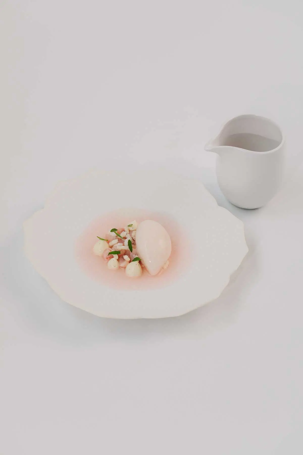 Pale quenelle over a rose-coloured broth with diced garnish, a porcelain jug alongside