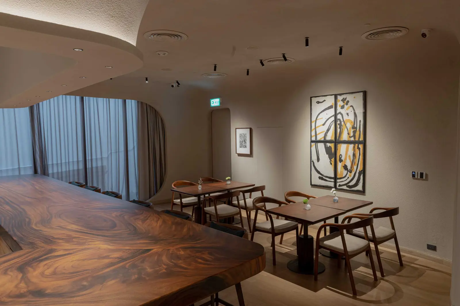 Dining room with a live-edge communal table, wooden chairs and a large black-and-yellow abstract painting