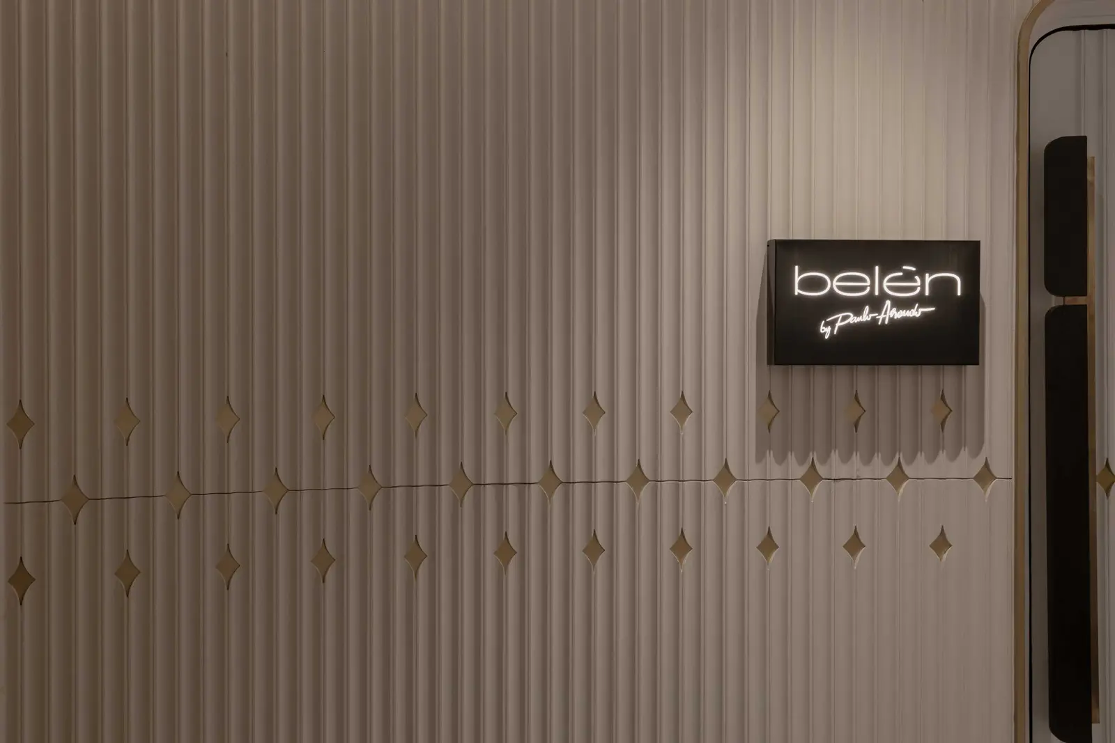 Illuminated Belén by Paulo Airaudo sign on a fluted wall with gold diamond tiles